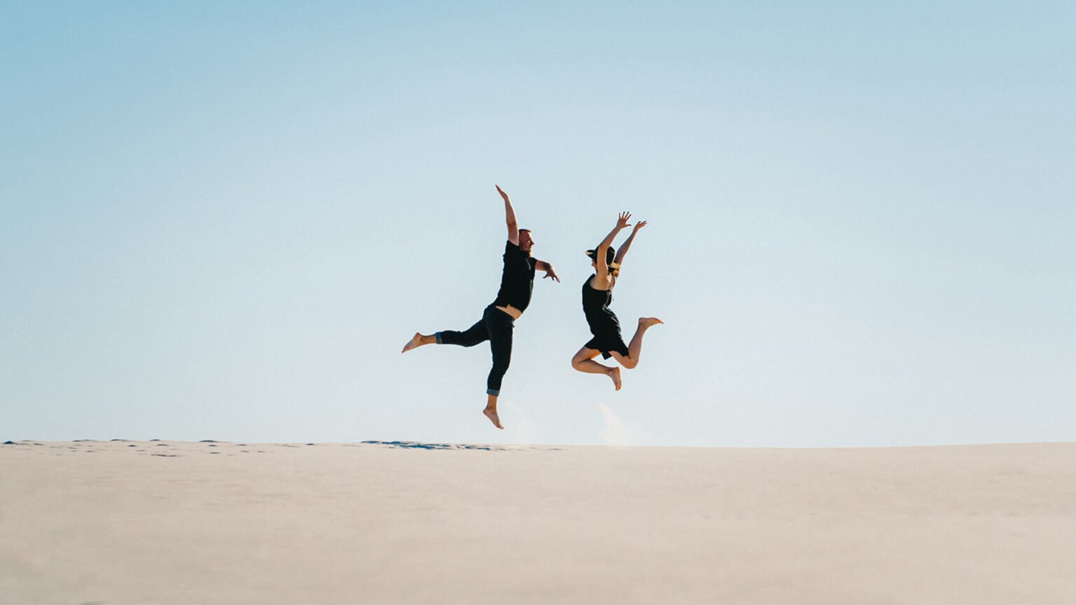 Couple jumping up high on a beach feeling positive benefits of raised NAD levels.