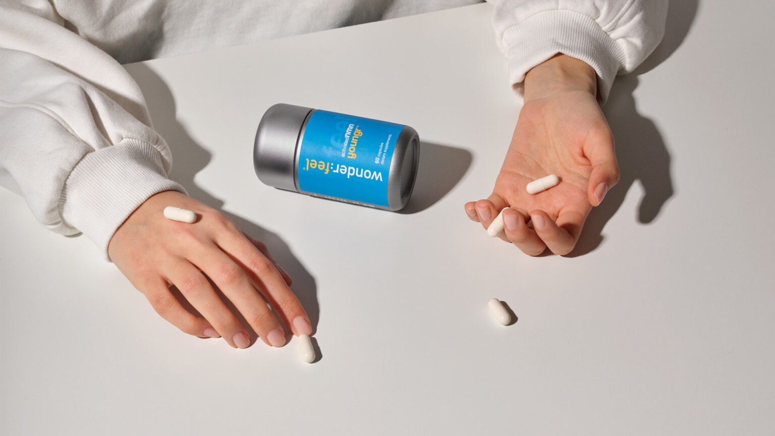 A Wonderfeel Youngr bottle and hands holding NMN capsules.
