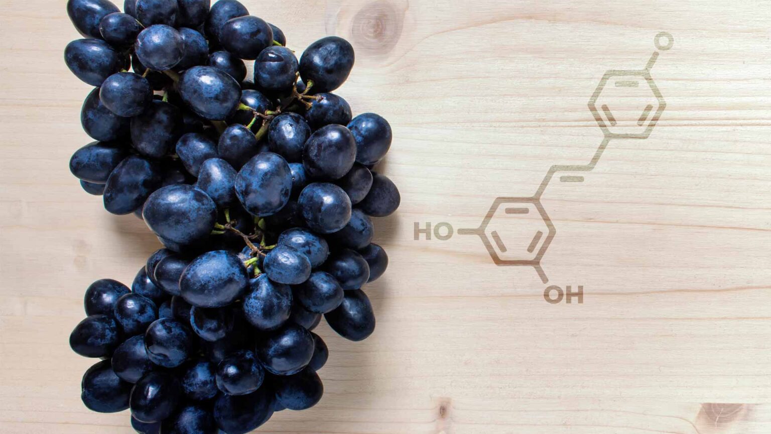 Dark skin grapes on a wood board with the molecular structure of resveratrol laser-etched into the surface.