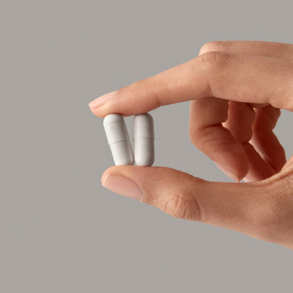 Two Youngr NMN capsules held between fingers representing the daily dose.