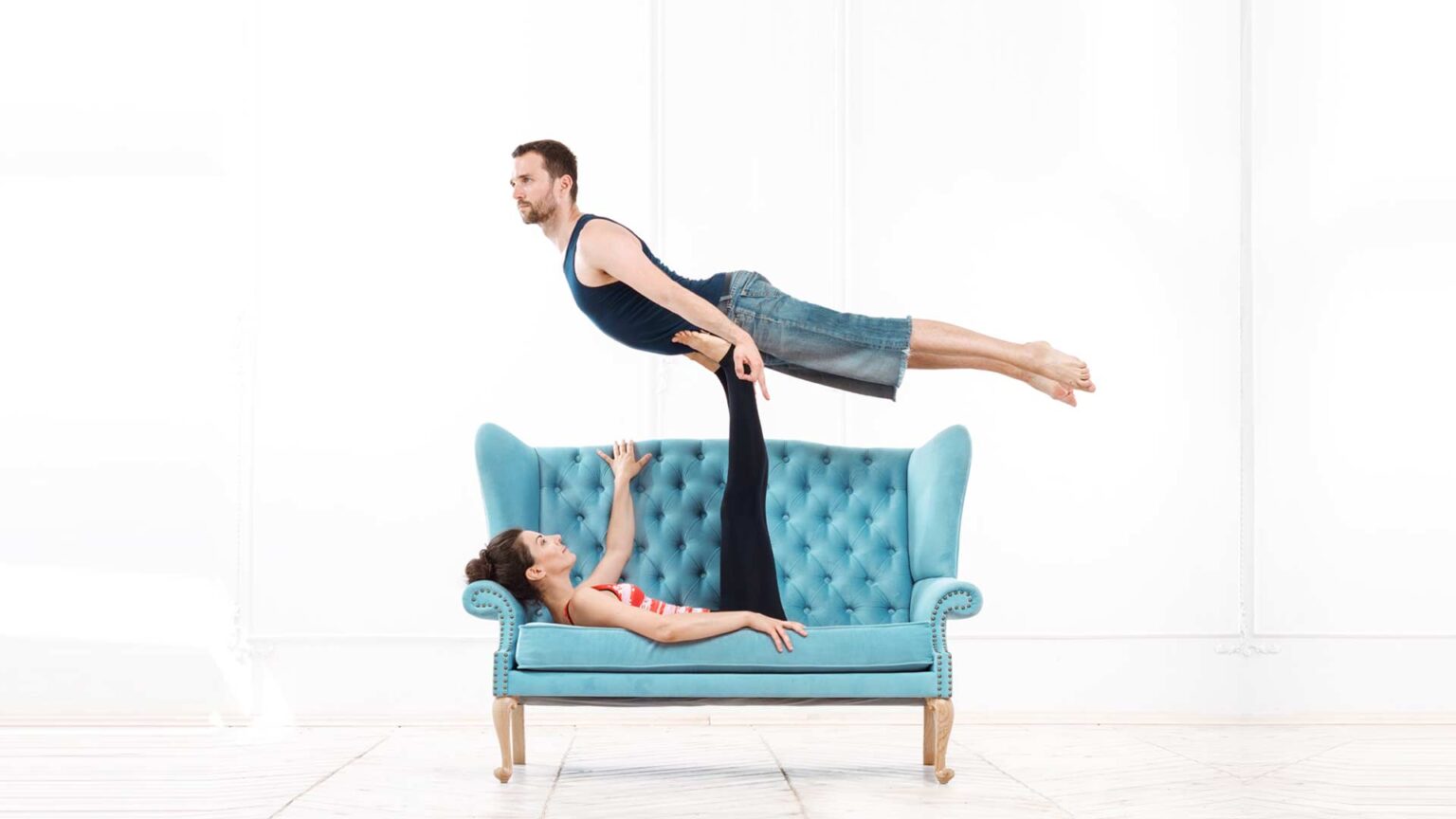 A couple practicing acro yoga on a blue chair